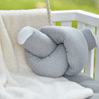 Eine KraftKids GmbH Wickeltischrolle Musselin grau Punkte mit weißen Enden sitzt auf einer cremefarbenen Decke auf einem weißen Kinderbett mit einer grauen Matratze. Grünzeug erscheint im Hintergrund verschwommen.