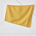 Ein KraftKids Sonnensegel Leinen gelb senfgelb hängt ungleichmäßig an einer weißen Holzwand mit schrägen Platten und einem sichtbaren schwarzen Metallscharnier.