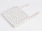 A KraftKids Sitzkissen für Stühle aus Musselin in hellem Creme mit feinem braunem Blattmuster und zwei Paar Stoffbändern auf einer Seite, rechteckig geformt, präsentiert auf weißem Hintergrund.