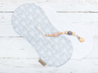 Das KraftKids Spucktuch weiße Pfeile auf Grau aus grauer Baumwolle mit weißen Pfeilmustern wird auf einem weißen Tuch auf einer hölzernen Unterlage präsentiert, auf der ein Schnullerclip aus Holz und Häkelperlen angebracht ist.