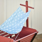 Ein KraftKids Sonnensegel "weiße Diamante auf Pastell Blau" mit weißen Rautenmustern ist über einen roten Holzwagen auf Sand drapiert, mit einem weißen Zaun im Hintergrund.