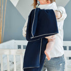 Eine Frau in einem Kinderzimmer hält ein Baby über der Schulter, die KraftKids Babydecke Musselin dunkelblau auf ihrem Rücken drapiert. Die Beine des Babys sind sichtbar, und im Hintergrund ist ein weißes Kinderbett zu sehen.