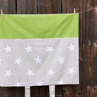 Der KraftKids Bezug für Wickeltischauflage "große weiße Sterne auf Beige, weiße Punkte auf Grün" aus 100% Baumwolle hängt mit zwei Klammern vor einem Holzzaun. Der Bezug ist abnehmbar und waschbar - ideal als Wickeltischauflagenbezug.