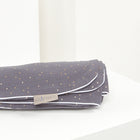 Die KraftKids Babydecke Musselin goldene Punkte auf Grau zeigt eine gefaltete graue Musselin-Decke mit goldenen Punkten, weißem Rand und einem KraftKids-Etikett auf einer weißen Fläche vor einem hellen Hintergrund.