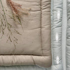 Beige und hellblaue Steppdecken mit abgesteppten Rändern sind übereinandergelegt und ähneln der KraftKids Wickelauflage Leinen Natur Braun. Auf dem beigen Quilt liegt eine getrocknete Pflanze, während der blaue Quilt darunter ein dezentes Punktmuster aufweist.