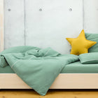 Ein ordentlich gemachtes Bett mit dem KraftKids Bettwäscheset Doppelkrepp Grün Jade und einem gelben Sternenkissen, vor einer grauen Betonwand und einem hellen Holzboden, schafft den perfekten Raum für erholsamen Schlaf.