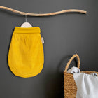 Ein KraftKids Strampelsack Frühling Sommer Cord Breitcord in Gelb Senf hängt an einem Holzast an einer dunklen Wand, neben einem geflochtenen Korb mit einer hellgrauen Decke, die über den Rand drapiert ist.