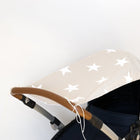 Eine Nahaufnahme des KraftKids Sonnensegels große weiße Sterne auf Beige mit einem beigen Verdeck mit großen weißen Sternen auf einem Kinderwagen mit braunem Griff hebt sich von einem schlichten weißen Hintergrund ab.