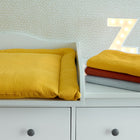 Eine weiße Kommode mit drei Schubladen enthält eine KraftKids Wickelauflage Doppelkrepp Gelb Senf und gestapelte Decken in Gelb, Rot und Grau. Im Hintergrund steht ein beleuchteter Buchstabe Z an einer gemusterten Wand.