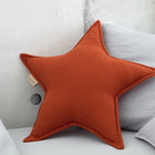 Ein weiches Sternkissen Doppelkrepp Rot Herbstrot von KraftKids ruht auf einer hellgrauen Couch, umgeben von passenden Kissen und vor einer Betonwand - ein idealer spielerischer Akzent für jedes Kinderzimmer.