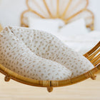 Eine Nahaufnahme des KraftKids qualitäts Stillkissen Musselin Zweige braun in einem Rattan-Hängesessel mit einem cremefarbenen und braunen Zweigmuster, mit einem Teil eines ergonomischen Bettgestells aus Korbgeflecht, das im hellen Raumhintergrund sanft verschwimmt.