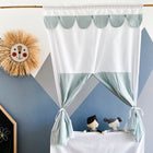 In einem gemütlichen Kinderzimmer steht das KraftKids Puppentheater Kasperletheater aus grünem Musselin mit goldenen Punkten, komplett mit Teleskopstange, vor einer geometrisch gemusterten Wand.