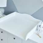 Ein KraftKids Wickelaufsatz Universal weiß durchgehender Boden steht auf einer Kommode, die mit einem ausgestopften Hasen, einer Bürste und einem Taschentuchbehälter dekoriert ist. Dahinter ist die Wand mit eleganten grauen und weißen geometrischen Mustern versehen.